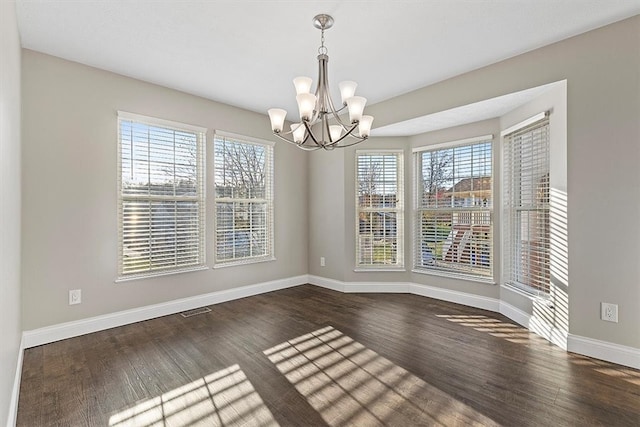 unfurnished dining area featuring dark hardwood / wood-style floors, plenty of natural light, and a notable chandelier