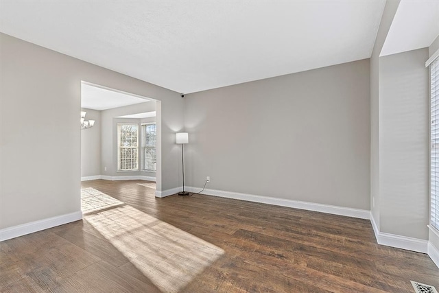 spare room with dark hardwood / wood-style flooring and a chandelier