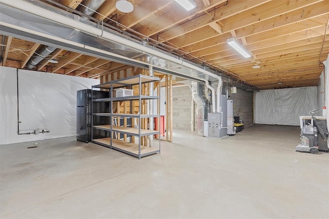 basement with black refrigerator, heating unit, and water heater