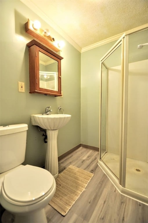 bathroom with wood-type flooring, toilet, a shower with door, and ornamental molding