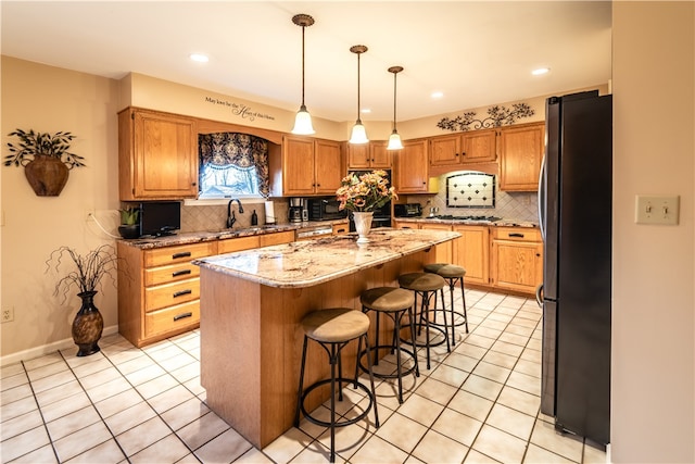 kitchen featuring light stone countertops, stainless steel fridge, sink, pendant lighting, and a center island