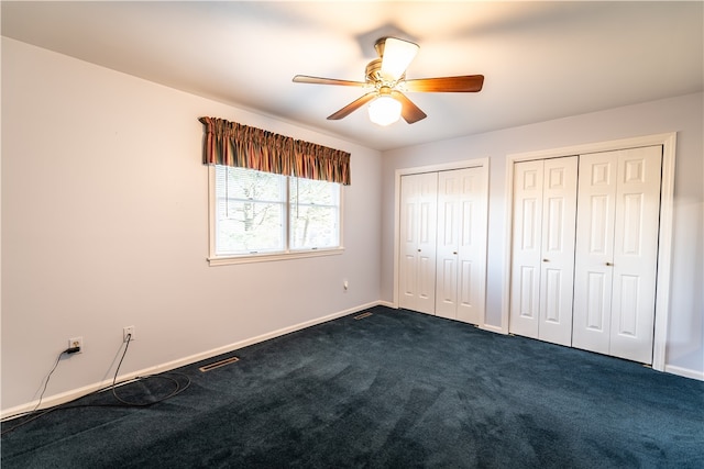 unfurnished bedroom featuring dark colored carpet, two closets, and ceiling fan