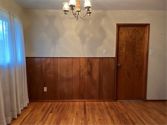 unfurnished room with wood walls, light hardwood / wood-style floors, and a notable chandelier