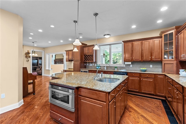 kitchen with sink, pendant lighting, a center island with sink, dark wood-type flooring, and light stone counters