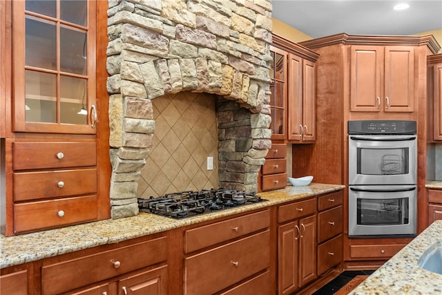 kitchen with decorative backsplash, stainless steel double oven, light stone counters, and black gas stovetop