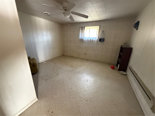 empty room with baseboard heating, ceiling fan, and wood walls