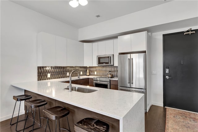 kitchen with kitchen peninsula, a kitchen breakfast bar, stainless steel appliances, sink, and white cabinets