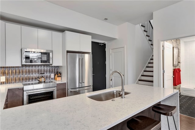 kitchen featuring white cabinetry, sink, tasteful backsplash, a kitchen bar, and appliances with stainless steel finishes