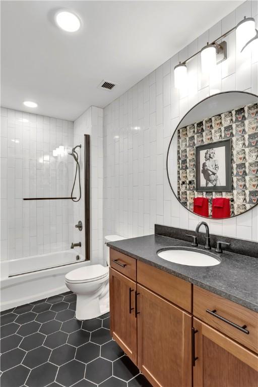 full bathroom featuring vanity, tile patterned floors, tiled shower / bath, toilet, and tile walls