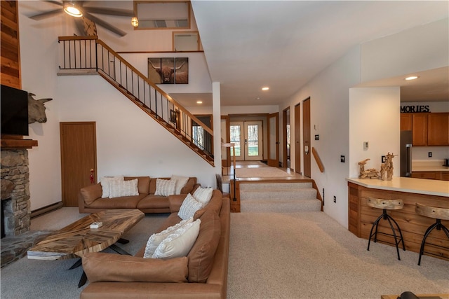 carpeted living room featuring french doors, a stone fireplace, and ceiling fan