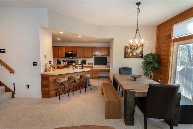 carpeted dining room featuring wooden walls, sink, and an inviting chandelier