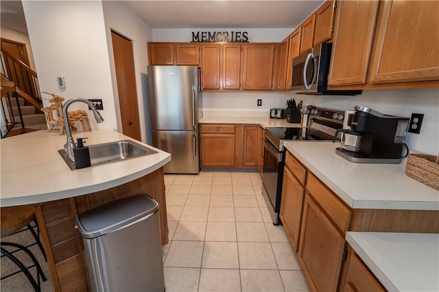 kitchen with light tile patterned flooring, sink, a kitchen bar, and stainless steel appliances