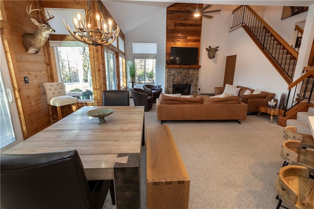 dining space with a notable chandelier, a stone fireplace, carpet floors, and high vaulted ceiling