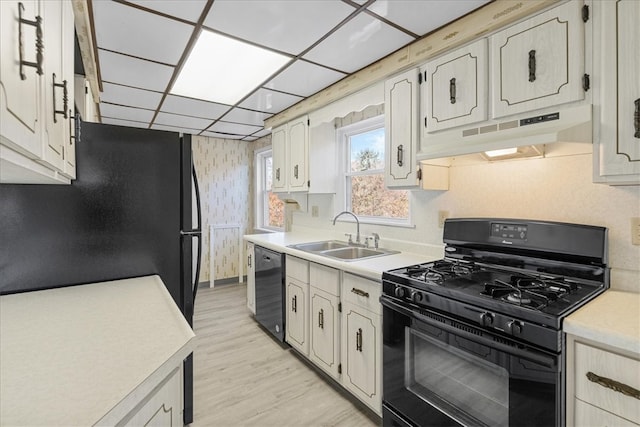 kitchen with a paneled ceiling, sink, black appliances, and light hardwood / wood-style floors