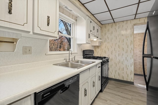 kitchen with a paneled ceiling, sink, black appliances, light hardwood / wood-style floors, and white cabinetry