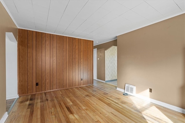 spare room with wooden walls, crown molding, and light hardwood / wood-style floors