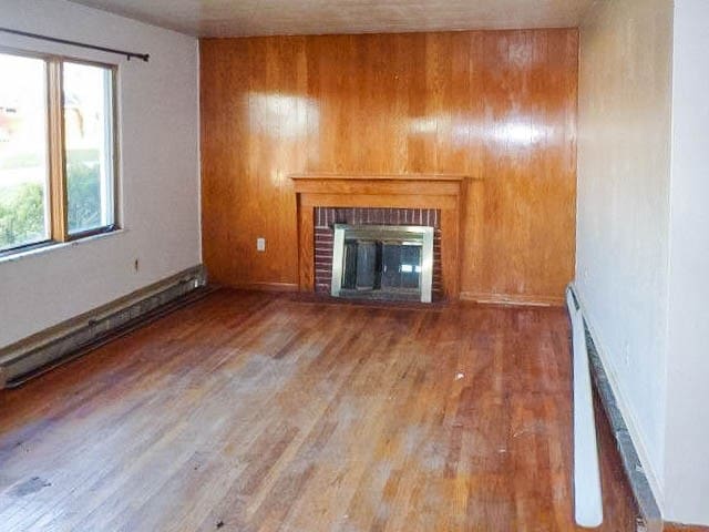 unfurnished living room with a fireplace, wood walls, and hardwood / wood-style flooring