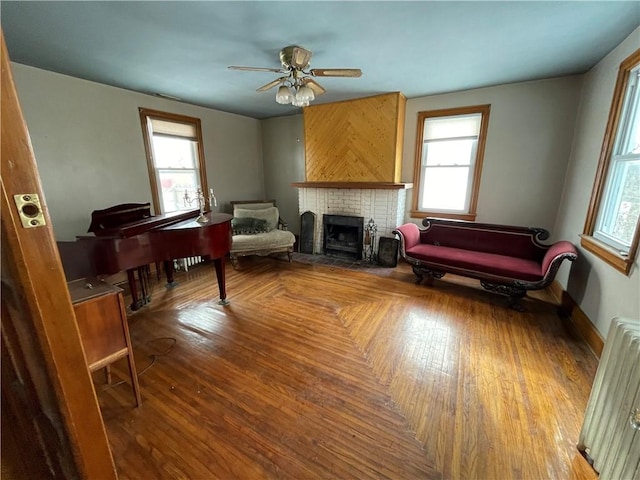 living area with radiator heating unit, a brick fireplace, plenty of natural light, and ceiling fan