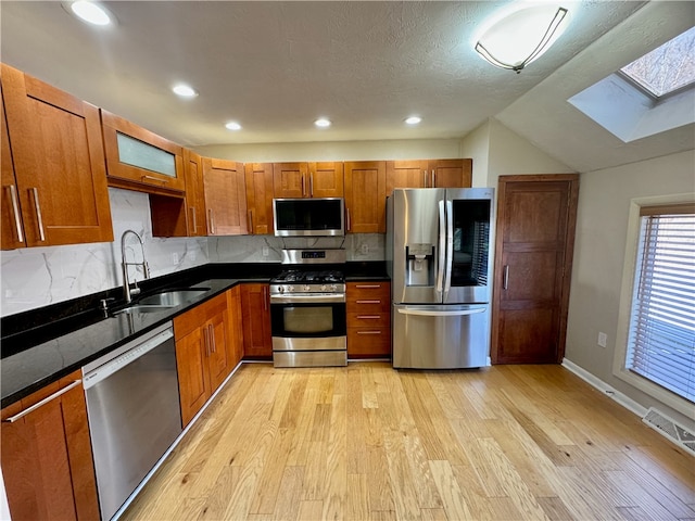 kitchen featuring sink, light hardwood / wood-style floors, decorative backsplash, vaulted ceiling with skylight, and appliances with stainless steel finishes