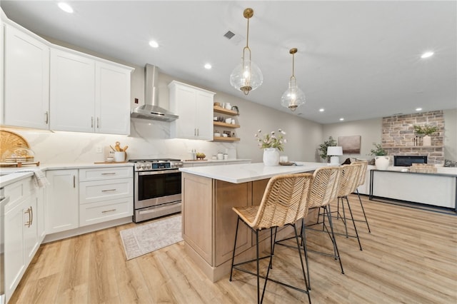 kitchen featuring white cabinetry, a center island, wall chimney exhaust hood, light hardwood / wood-style flooring, and stainless steel stove