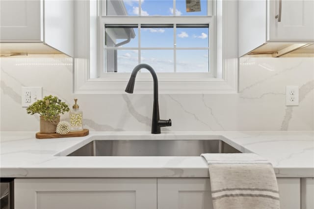 details with white cabinets, backsplash, light stone countertops, and sink