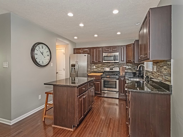 kitchen featuring sink, dark wood-type flooring, stainless steel appliances, a breakfast bar, and a kitchen island