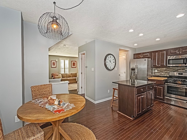 kitchen with a textured ceiling, dark hardwood / wood-style flooring, stainless steel appliances, and a kitchen island