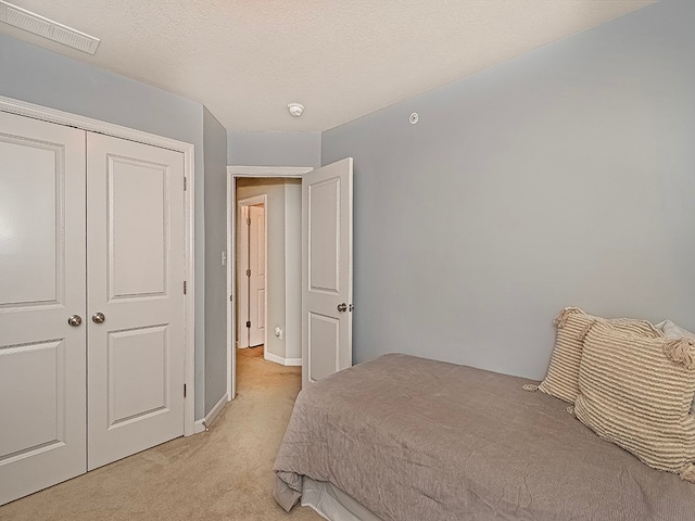 bedroom featuring light colored carpet, a textured ceiling, and a closet