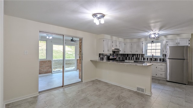 kitchen featuring light stone countertops, tasteful backsplash, kitchen peninsula, white cabinets, and appliances with stainless steel finishes