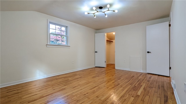 unfurnished bedroom with a spacious closet, a closet, vaulted ceiling, and light wood-type flooring