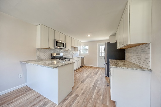 kitchen with sink, light hardwood / wood-style flooring, light stone countertops, appliances with stainless steel finishes, and white cabinetry