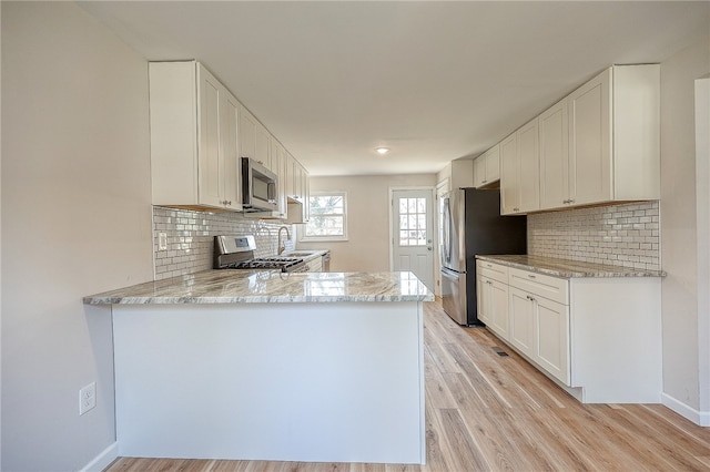 kitchen featuring kitchen peninsula, appliances with stainless steel finishes, light wood-type flooring, decorative backsplash, and white cabinets