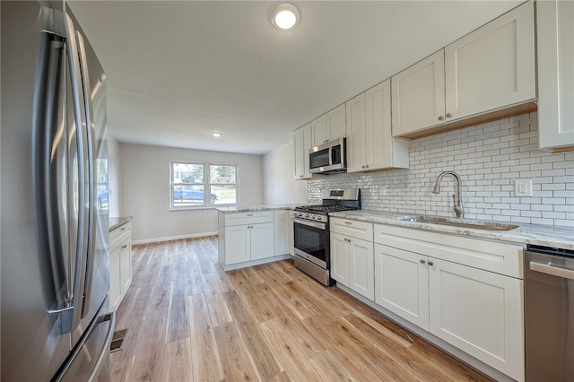 kitchen featuring light stone countertops, white cabinetry, sink, light hardwood / wood-style floors, and appliances with stainless steel finishes