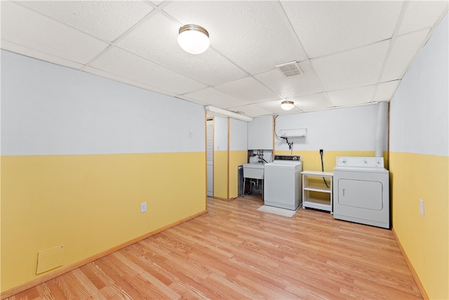 clothes washing area with washing machine and dryer, sink, and light hardwood / wood-style flooring