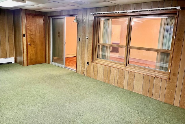 carpeted spare room featuring a paneled ceiling, baseboard heating, and wooden walls