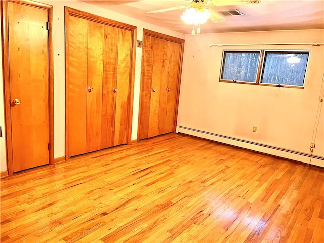 unfurnished bedroom featuring ceiling fan, light hardwood / wood-style floors, baseboard heating, and two closets