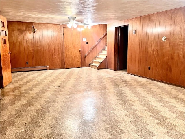 basement with ceiling fan, a textured ceiling, wooden walls, and a baseboard heating unit