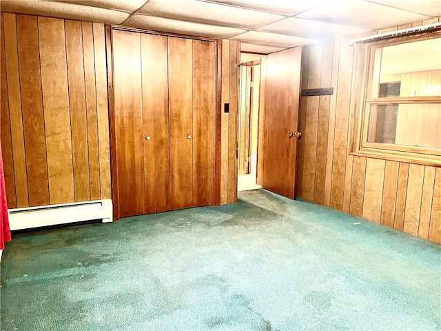 interior space with a paneled ceiling, wood walls, and a baseboard radiator