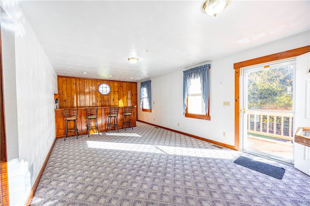 unfurnished living room featuring wooden walls, light colored carpet, and indoor bar