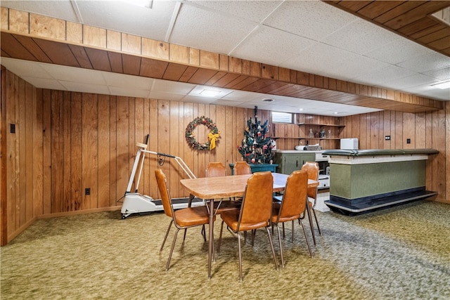 dining space with carpet flooring, a drop ceiling, and wood walls