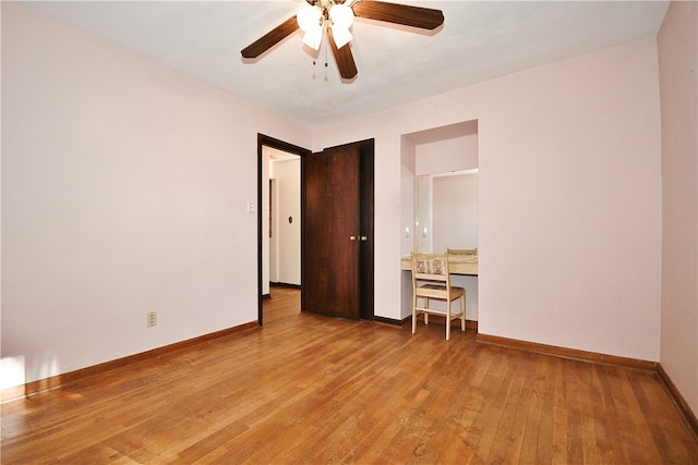 unfurnished bedroom with ceiling fan, built in desk, and light wood-type flooring