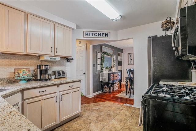 kitchen with backsplash, black range with gas stovetop, light wood-type flooring, light brown cabinetry, and light stone counters