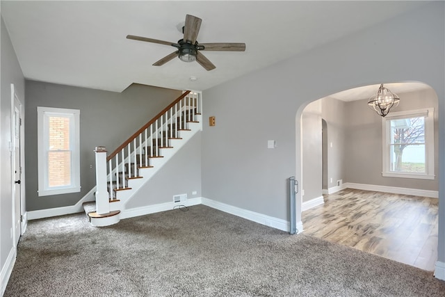 unfurnished living room featuring hardwood / wood-style floors, ceiling fan with notable chandelier, and a wealth of natural light