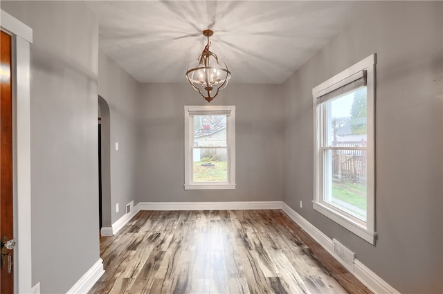 unfurnished room featuring plenty of natural light, wood-type flooring, and a notable chandelier