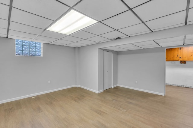 basement with a paneled ceiling and light wood-type flooring