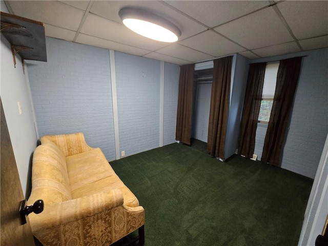 sitting room featuring dark colored carpet, a paneled ceiling, and brick wall