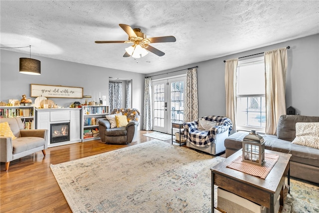 living room featuring ceiling fan, french doors, a textured ceiling, and light hardwood / wood-style flooring