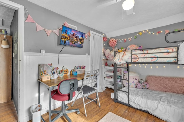 bedroom featuring a textured ceiling, hardwood / wood-style flooring, ceiling fan, and wood walls