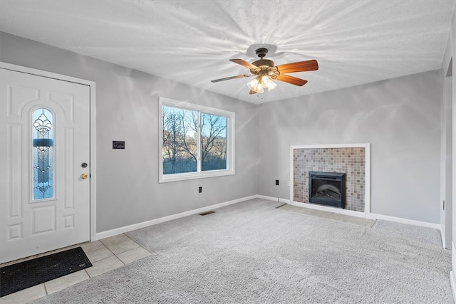 unfurnished living room with light carpet, a fireplace, ceiling fan, and a textured ceiling