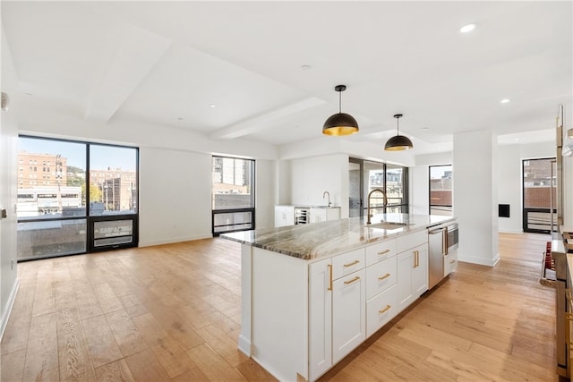 kitchen with white cabinets, sink, hanging light fixtures, light hardwood / wood-style flooring, and light stone counters